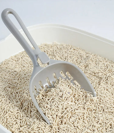 A KittyNook Cat Co. Curved Cat Litter Shovel sits in a box of odor-free, pellet cat litter.